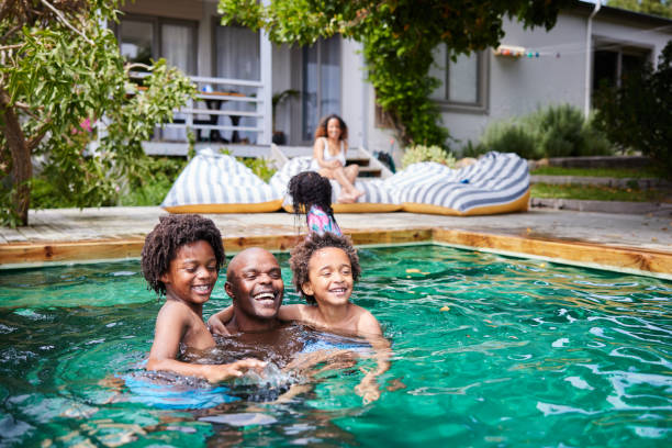Dad playing with his kids in a pool with their mom watching in summer