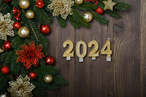 Happy New Year 2024 greeting card. Candle numbers on wooden background and layout of Christmas tree, balls, gifts. Close up and copy space, Selective focus.