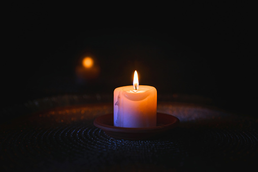 A burning candle.Bright light on dark background.RIP darkness template. lighting a candle in the darkness.the reflection of the candle in the dark mirror.