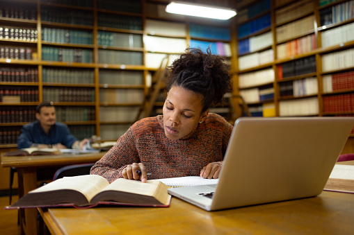 Young African American female student studying from a book in a library.