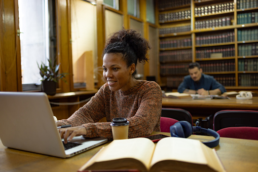 Happy African American college student surfing the Internet on a computer in a library.