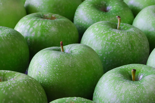 Stock photo showing close-up view of a group of green Granny Smith apples with shiny, speckled skin on green surface.
