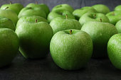 Close-up image of group of green Granny Smith apples (Malus domestica) with stalks, glossy, speckled skinned pieces of fruit, mottled dark grey background, focus on foreground