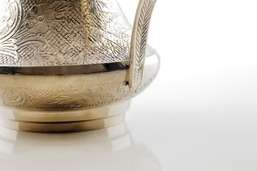 A close up crop of an ornate dallah which is a metal pot with a long spout designed specifically for making Arabic coffee