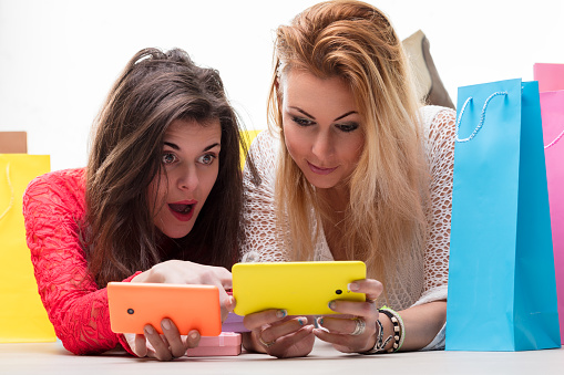 Friends compare purchases and share excitement over a shopping spree, smartphones in hand