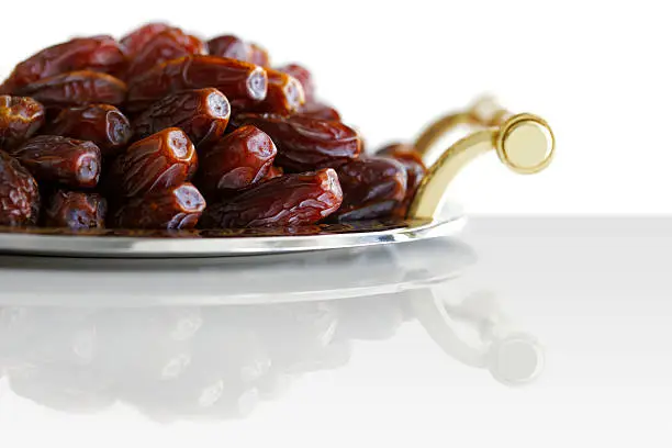 Dried Arabic dates presented on an ornate tray and shot against a white background