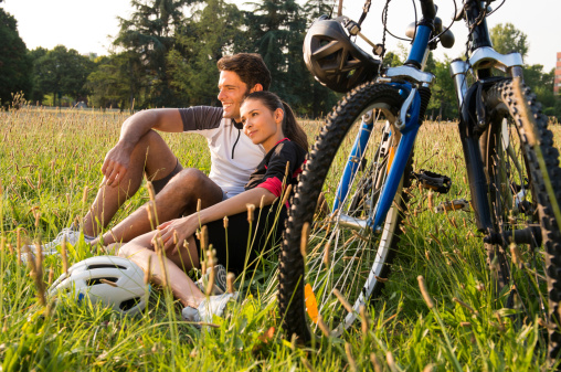 Relaxed Young Couple Sitting In Meadow Near Bicycles.