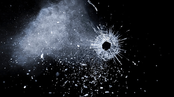 Close-up of bullet hole on glass against black background.