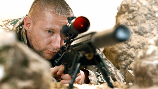 Close-up of soldier firing machine gun during battle surrounded by rocks.