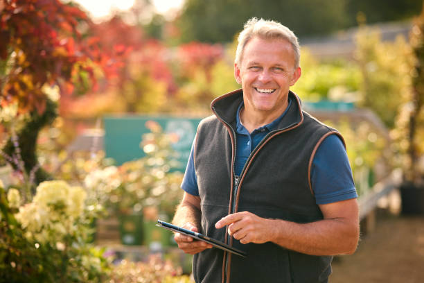 Portrait Of Mature Man Working Outdoors In Garden Centre Using Digital Tablet