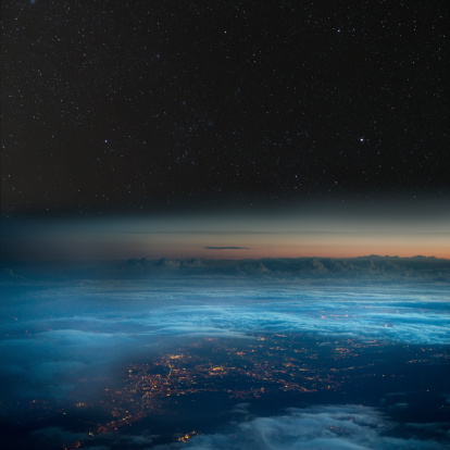 City lights below the clouds, stars above. Taken from a commercial flight.
