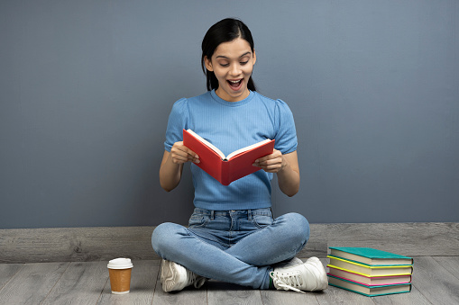 Surprised young woman reading a book at the library