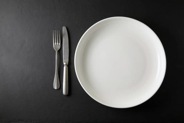 Empty white dinner plate and cutlery on a black stone table. Top view with copy space