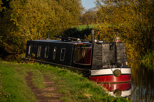 This is a narrow boat houseboat barge moored on the canal waterway nr. Stratford upon Avon. It is a warm sunny day in autumn and there are no visible people in the picture.