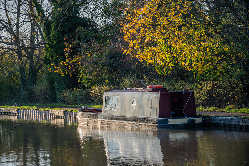 This is a narrow boat houseboat barge moored on the canal waterway nr. Stratford upon Avon. It is a warm sunny day in autumn and there are no visible people in the picture.