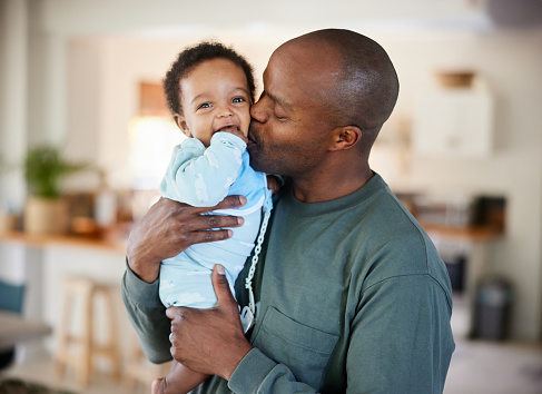 Loving father kissing his his adorable baby boy on the cheek while standing in their living room at home