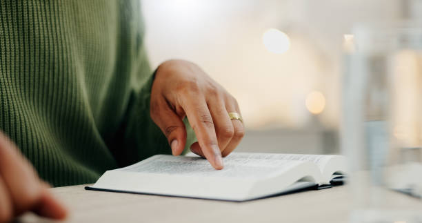 istock Closeup hand, reading and a bible for faith, spiritual support or hope from scripture. House, table and a person with a book for worship, trust or education on God, Jesus or learning about religion 1847087532