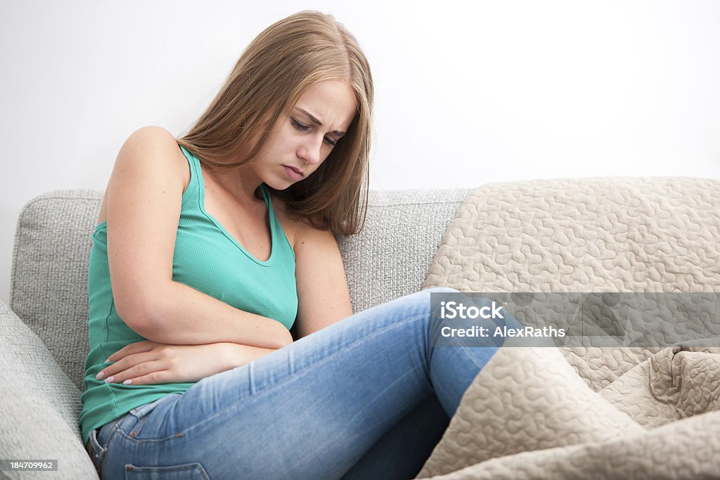 Young girl sitting on a sofa holding her stomach in pain Woman having abdominal pain, upset stomach or menstrual cramps Abdomen Stock Photo