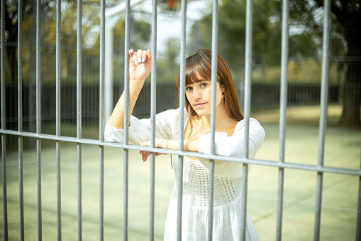 A captivating portrait of a young Caucasian woman with red hair and freckles, leaning behind a basketball court fence, looking directly at the camera.
