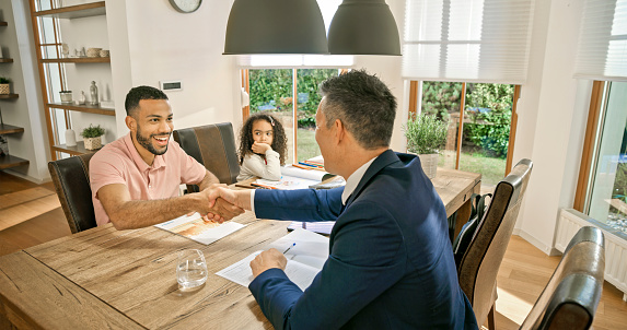 Smiling man and insurance agent handshaking after signing insurance documents as they sit at dining table.