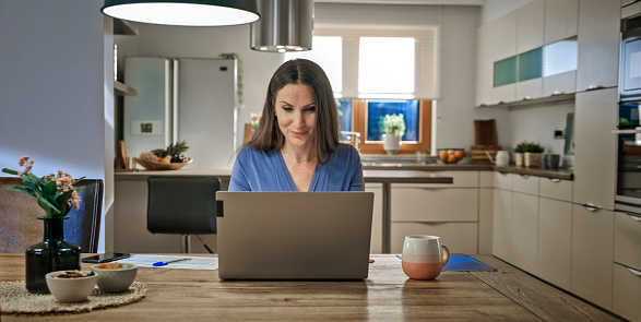 Smiling mature woman working on laptop while sitting in domestic room.