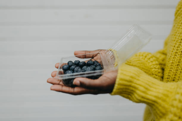 Top view, Female hands holding blueberry in the plastic box on light orange background, Vitamin-rich fruits are packed in boxes.