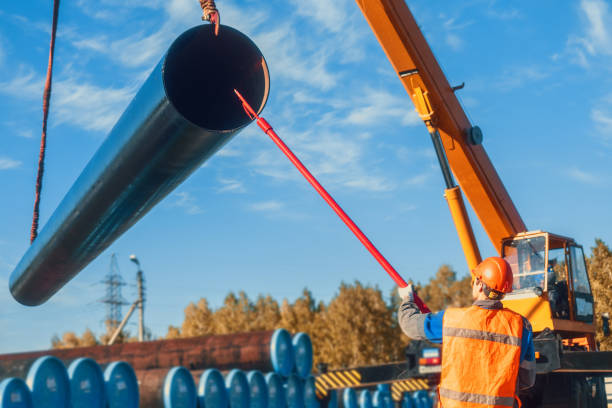 istock Professional slinger unloads large pipes for gasification on summer day in open warehouse. Supplier of gas equipment 1847155290