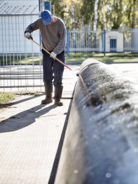istock Man handyman paints large diameter metal pipe outside with paint roller on summer day. Protection of metal from corrosion 1847162382