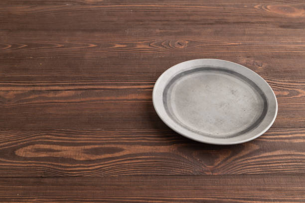 istock Empty gray ceramic plate on brown wooden. Side view, copy space 1847197370