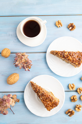 Walnut and hazelnut cake with caramel cream, cup of coffee on blue wooden background. top view, flat lay, close up