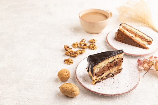 Chocolate biscuit cake with caramel cream and walnuts, cup of coffee on gray concrete background. side view, copy space.