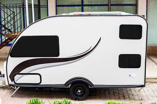 Caravan trailer for camping in the city. White big trailer with black wavy line and black windows outdoors