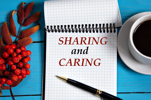 SHARING and CARING - words in a white notebook on a wooden blue background with a rowan branch and a fragment of a cup of coffee. Info concept