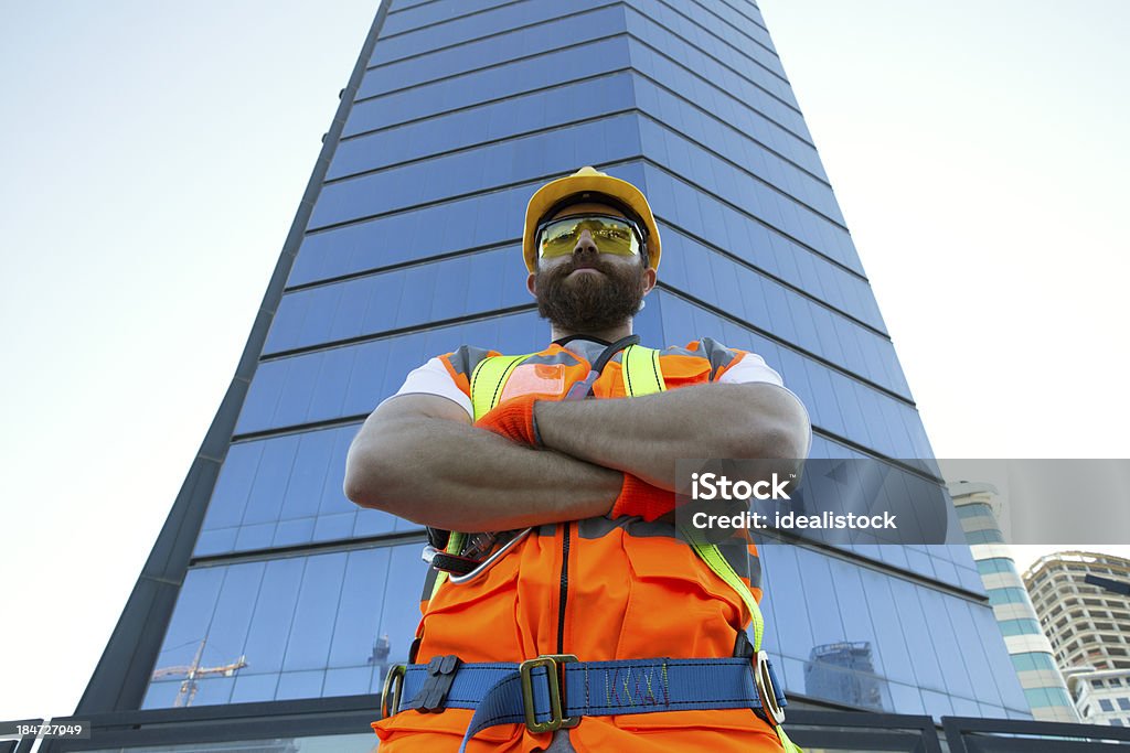 Construction Worker Construction worker standing in front of a skyscraper with his arms folded. Construction Industry Stock Photo