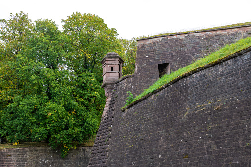 Picture of the citadel of Belfort in France. On the right side you can see a massive wall and a lookout tower. In the background are trees above the wall