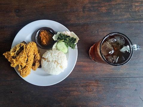 Ayam Goreng Kremes Or Crispy Fried Chicken With Crispy Spiced Flakes, Rice, Cucumber Sliced, Cabbage, Boiled Cassava Leaves, Chili Sauce And Fresh Tea Iced (Es Teh Segar). Food And Drink Menu.