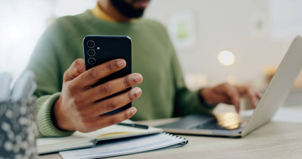 istock Phone, laptop and hands multitask or typing for work, online and man with project notebook on desk. Cellphone, app and businessman check information, email or research notes on internet and computer 1847284363