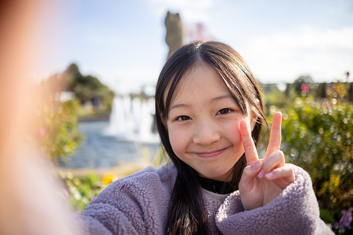 Teenage girl taking selfie picture in public park - peace sign