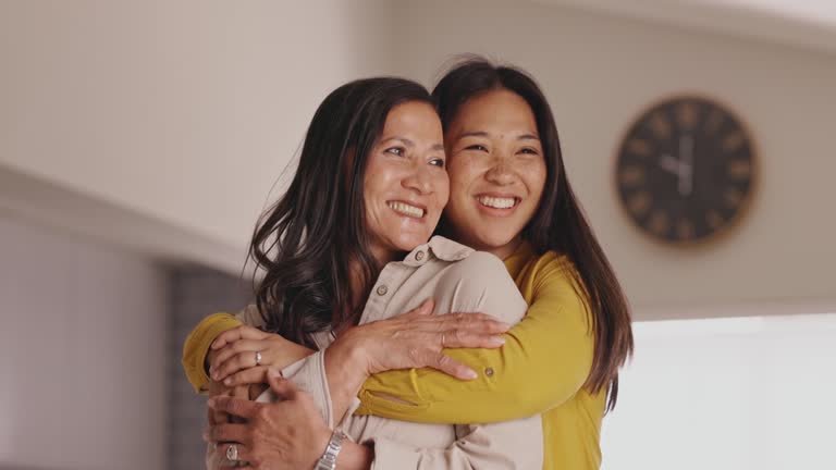 Portrait of happy mother and daughter hugging affectionately, looking sideways at home