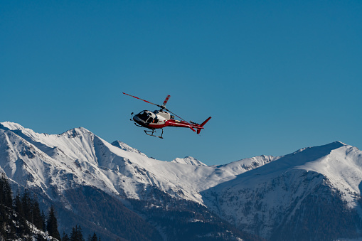 An Airbus Helicopter equipped for work flights in mid-flight in front of a snow-covered mountain panorama in the Swiss Alps