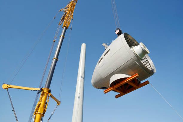 Large mobile crane picking up rotor hubcap gear equipment for a new wind turbine. Low angle view, taken under clear sky in the German North Sea Region, Lower Saxony, Germany, Europe.