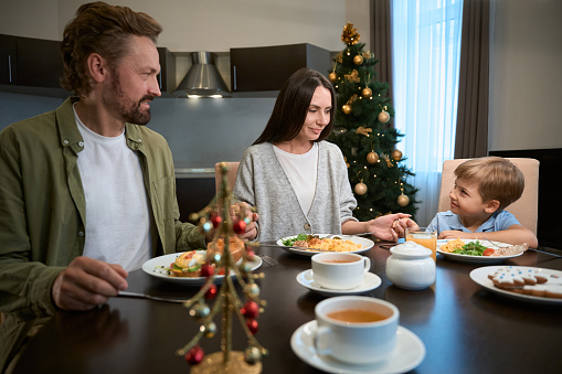 Joyful family holding hands and praying before festive Christmas dinner at home