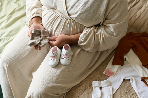 High angle view of pregnant woman preparing for childbirth, she sitting on bed and putting child clothes in order