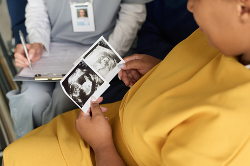 Close-up of pregnant woman looking at ultrasound image of her baby while having meeting with nurse