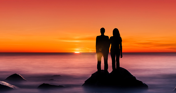 Sihouette of a man and a woman on a cliff at sunset