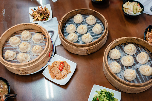 A table of Taiwanese cuisine, featuring three steamers of Xiaolongbao (soup dumplings) and several small side dishes.