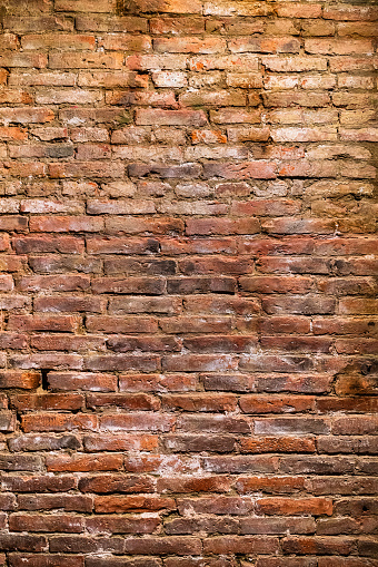 An old, crumbling red brick wall, uneven in color and filled with scratches.