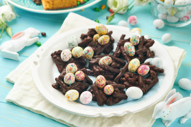 istock Easter chocolate nest cake with mini chocolate candy eggs with blossoming cherry or apple flowers on blue background table. Creative recipe for Easter table with holiday decorations. Top view. 1847453599