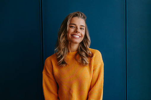 Beautiful young blond hair woman in yellow sweater smiling on blue background