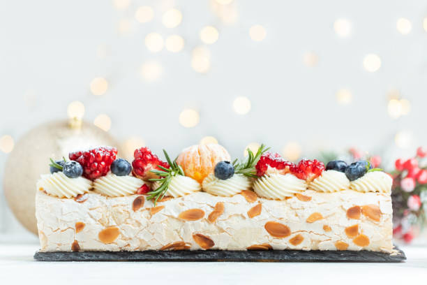 istock Meringue roll sprinkled with powdered sugar decorated with blueberries, pomegranate and almond flakes on the white background with blurred bokeh lights. Christmas festive pastry 1847514885
